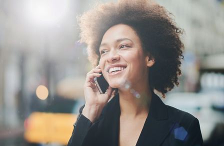 Smiling woman on street speaking to customer service on mobile phone