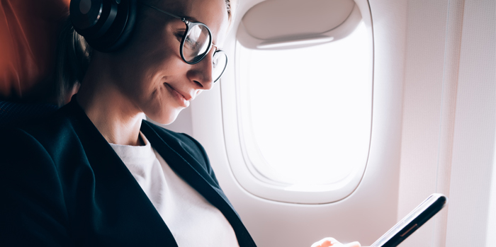 Traveler experiencing good wellbeing on a flight using her phone and wearing headphones