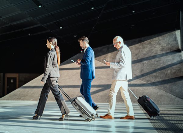 Three business travelers walking and wheeling their luggage